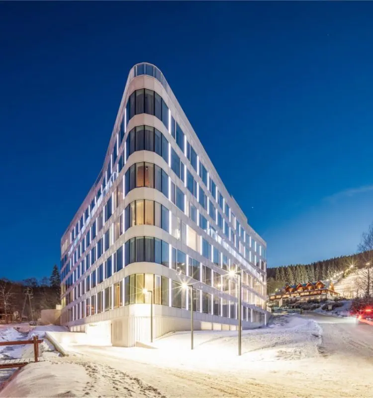 A well-lit hotel building in a triangular form of architecture, standing out in a winter forest background