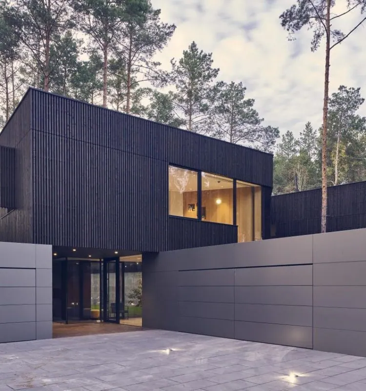 A modern minimalist home A modern minimalist looking luxurious home with concrete driveway, surrounded by tall trees.