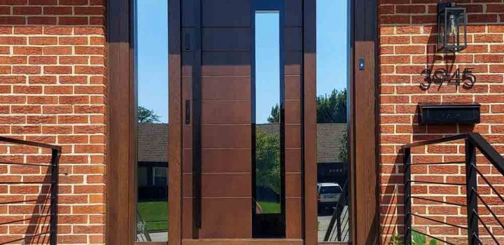 Main door of a house made of wood with two sidelights having reflective glass, a metal bar handle and two locksets