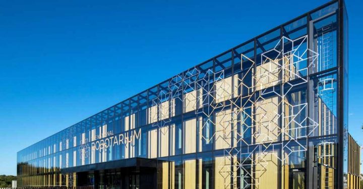 A modern architectural design of a building intended as a center of robotics and artificial intelligence, with glass facade and wide main entrance from a bridge.
